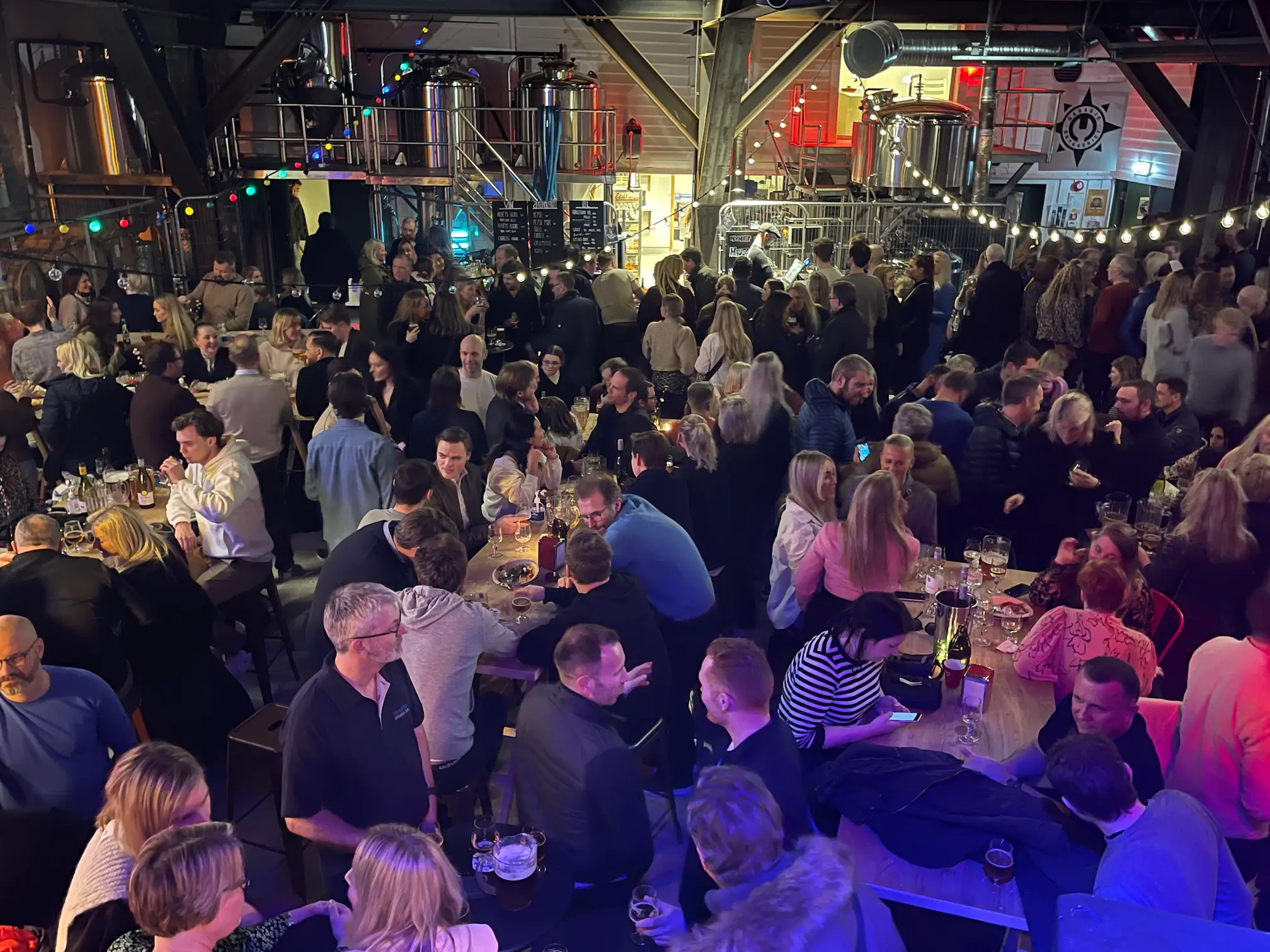 Fullt hus i garasjen på Høvleriet under FredagsPlease!, med bryggetankene på mezzaninen i bakgrunnen.